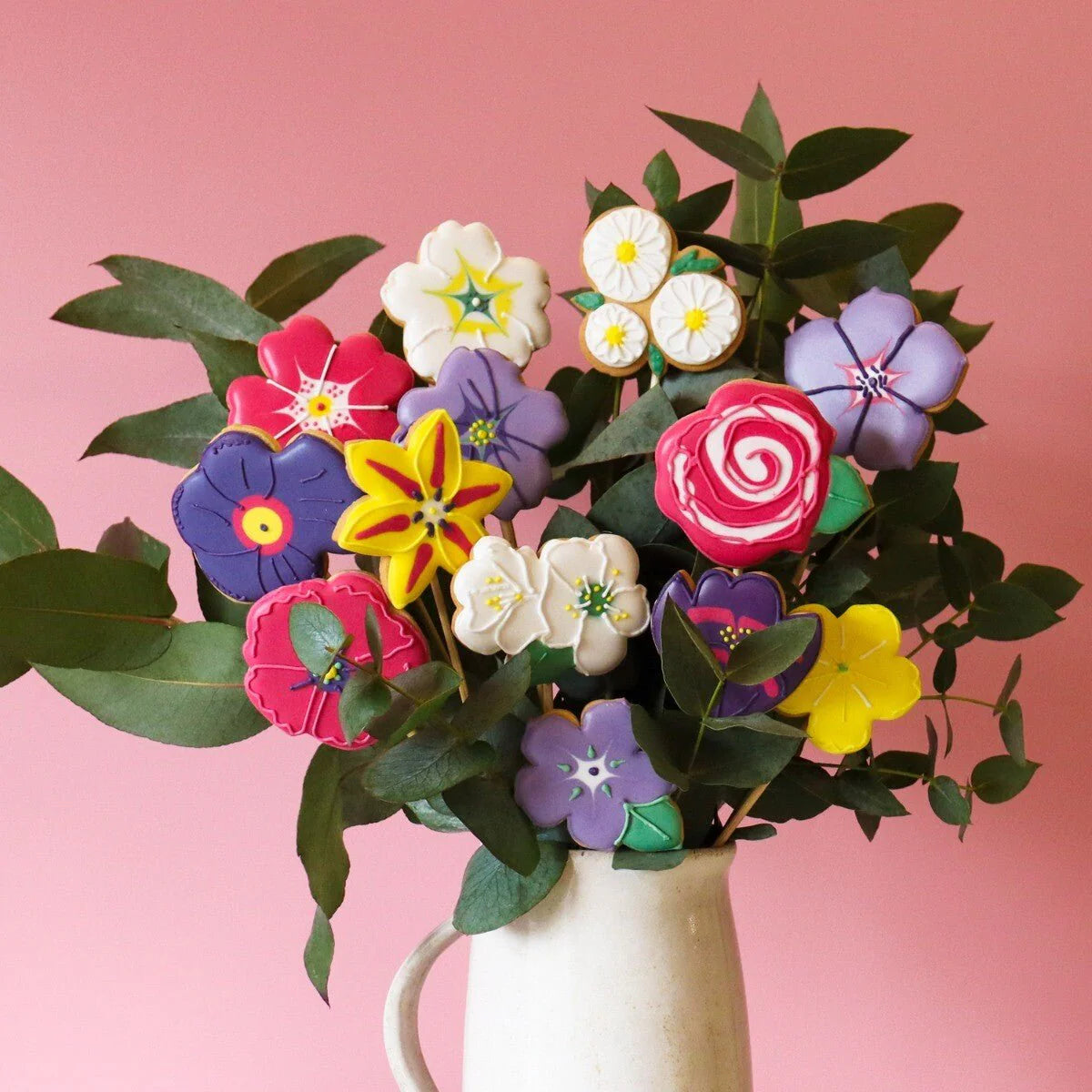 Bouquet of colorful flower-shaped cookies in a white vase on a pink background