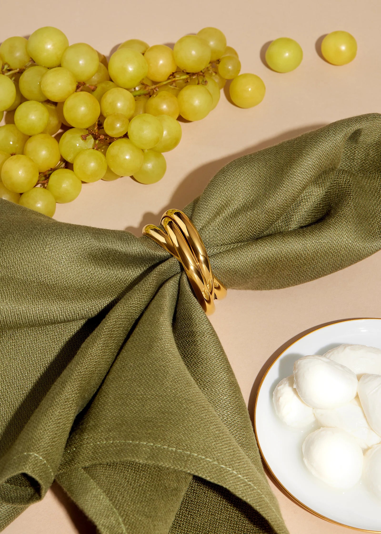 Green napkin with a gold napkin ring, grapes, and a bowl of white flowers on a beige background