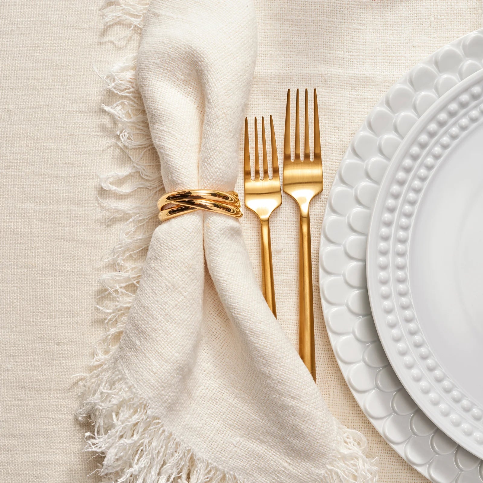 Gold cutlery set on a white napkin with a textured beige surface