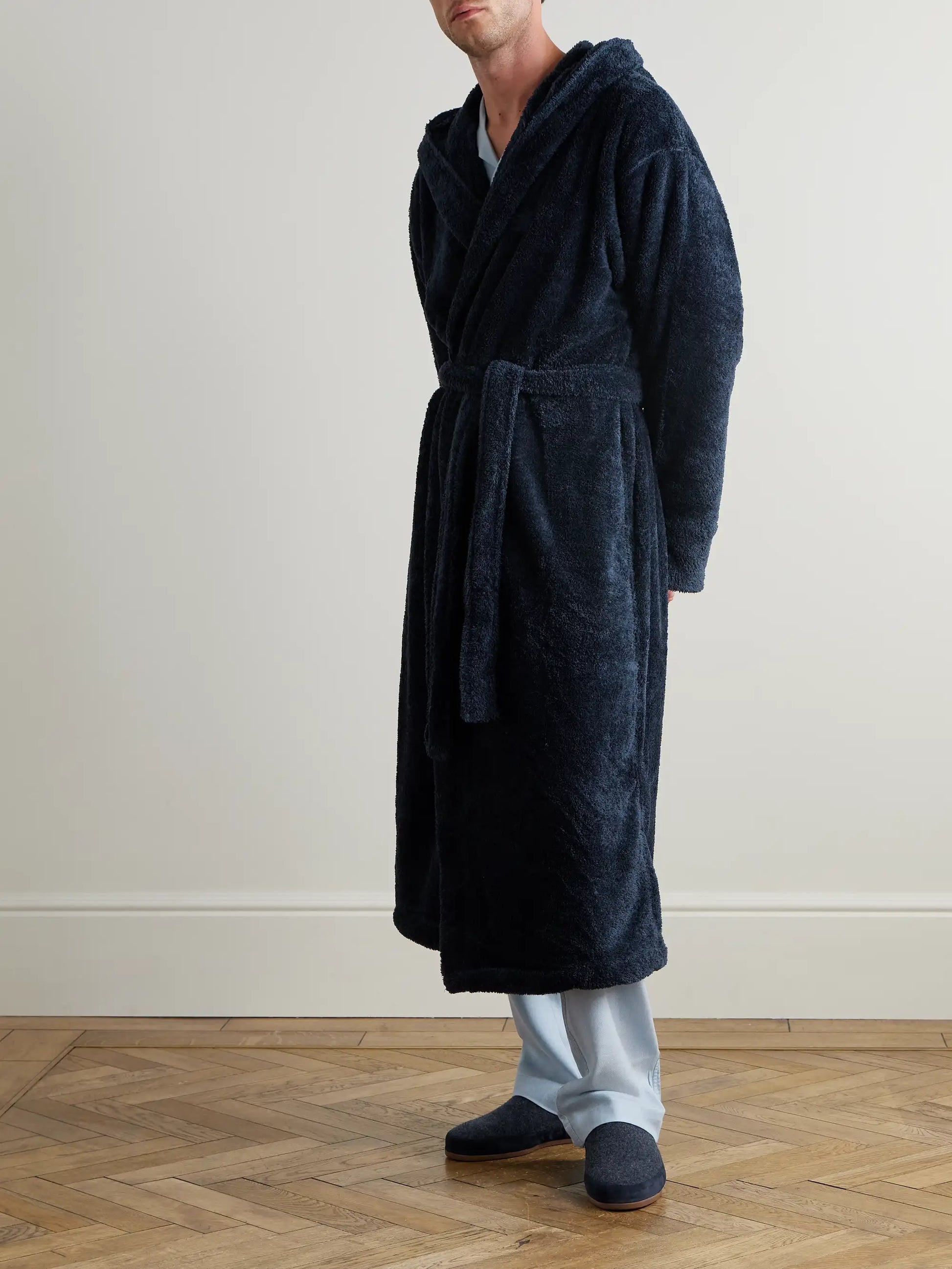 Person wearing a dark blue robe standing on a wooden floor.