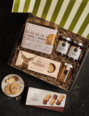 Gift basket with M&S products including jars, a box of shortbread, and cookies on a dark surface.
