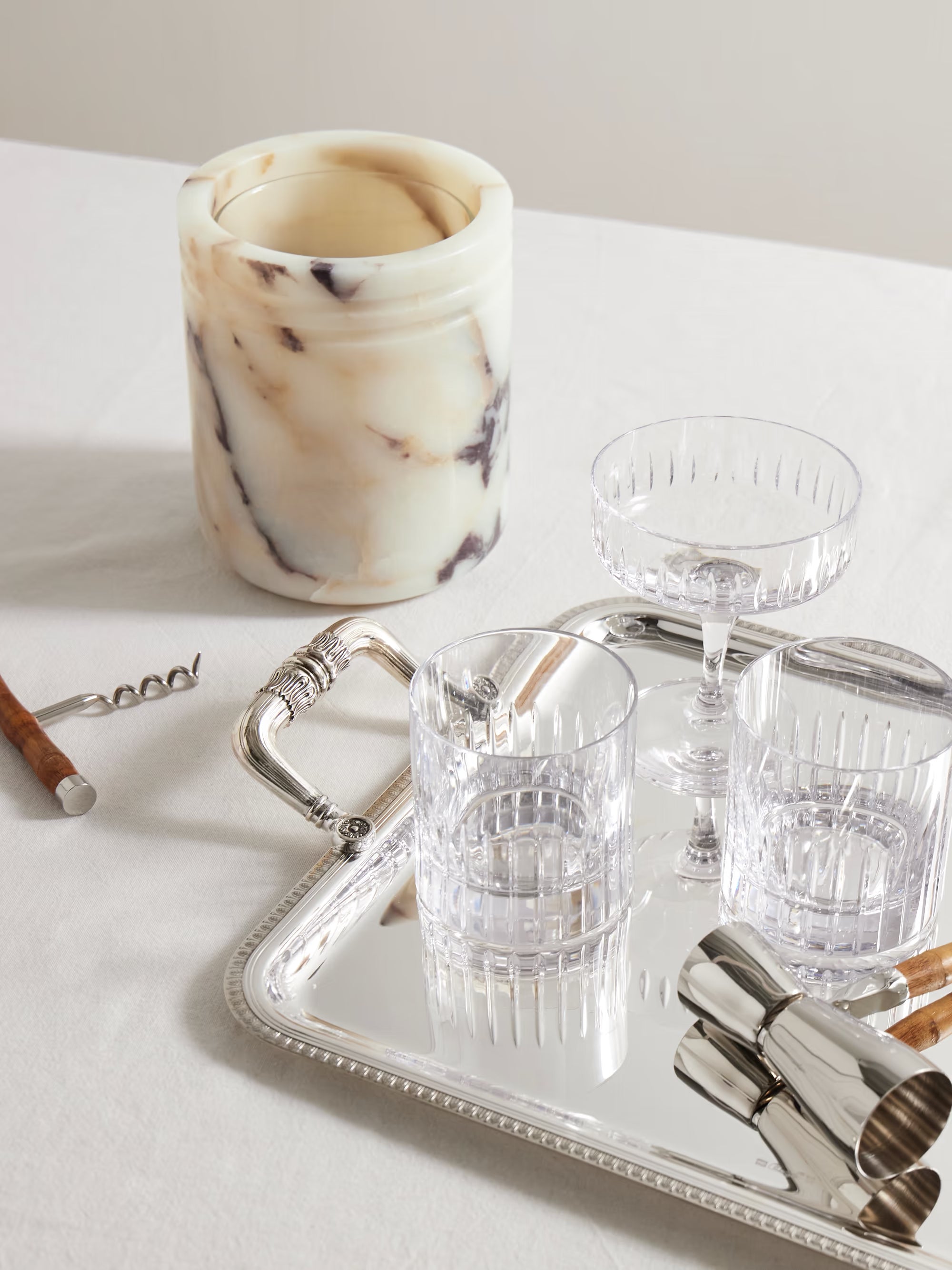 Cocktail glasses, a candle, and bar tools on a tray with a neutral background